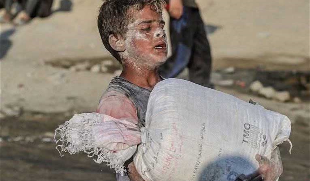 طفل فلسطيني يحمل كيس من طحين المساعدات في غزة