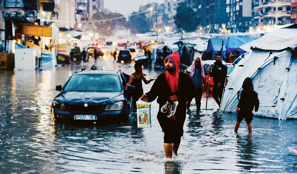 فلسطنيون يسيرون وسط مياه الامطار التي غمرت خيامهم في غزة