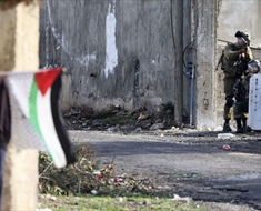 فلسطيني يرفع علم بلاده من خلف جدار في مواجهة جنود الاحتلال